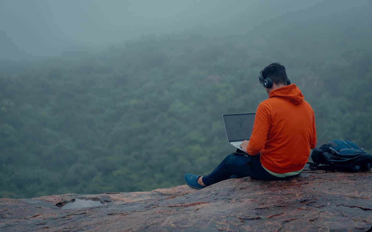Man in hoodie working on laptop in misty forest, Bengaluru. Modern remote work.